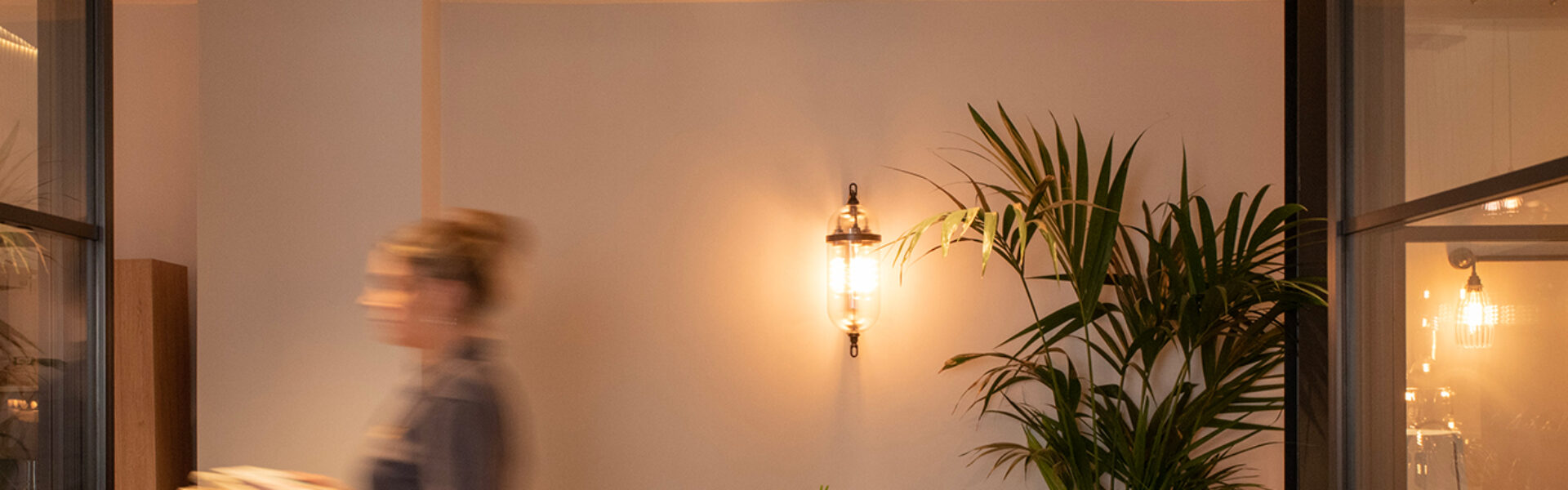 Lady walks across on office with office lighting including an Aston Wall Light and a Ribbed Upton wall light on conduit