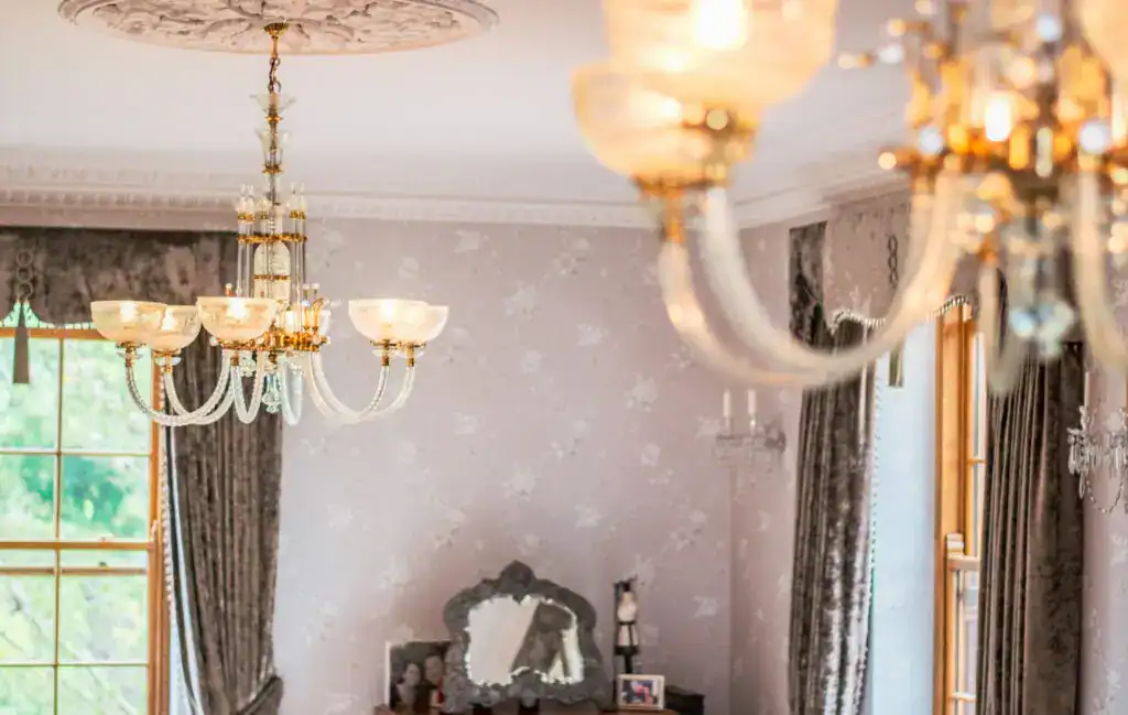 Elegant chandelier lighting in a classic living room with large windows and ornate curtains.
