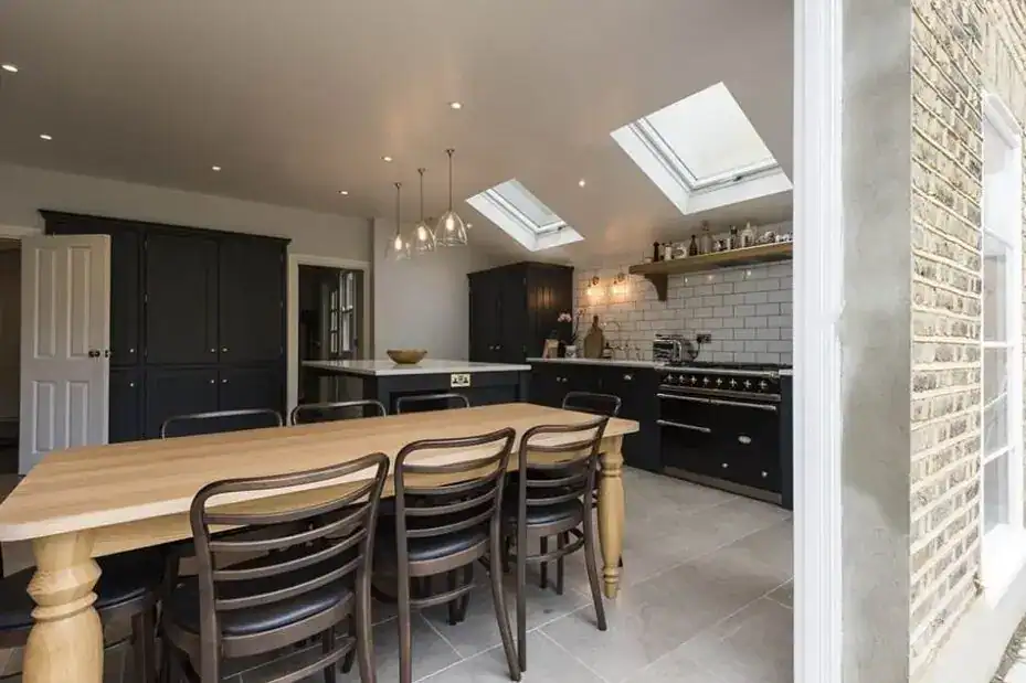 Bright modern kitchen featuring skylights, black cabinetry, and a wooden dining table with six chair.