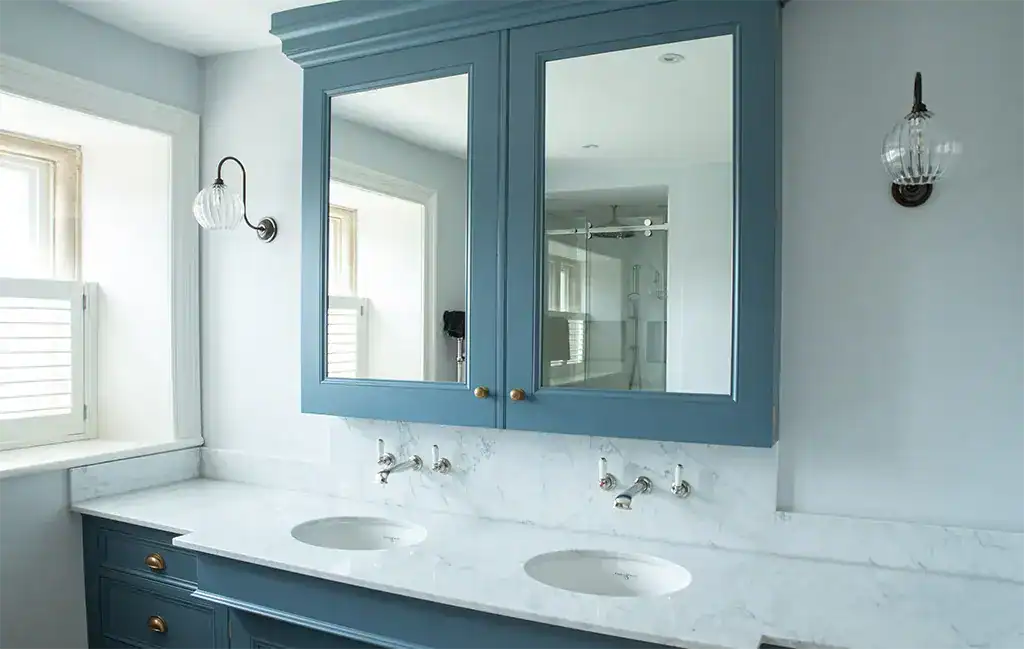 Blue bathroom vanity with double sinks and mirrored cabinet, featuring elegant lighting fixtures.