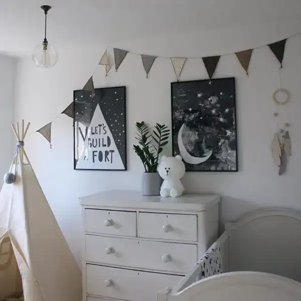 Nursery wall decor with bunting, framed moon and star art, and plush teddy bear.