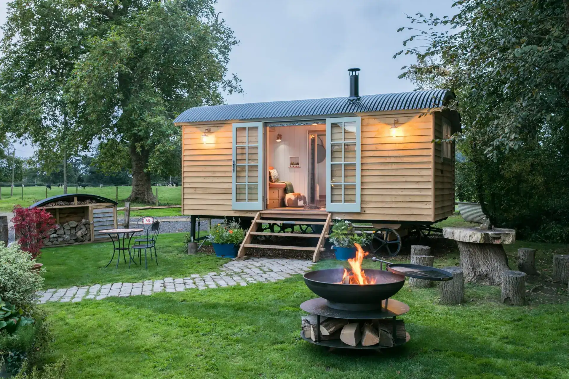 Cozy wooden garden cabin illuminated with warm exterior lighting, set in a lush green outdoor space.