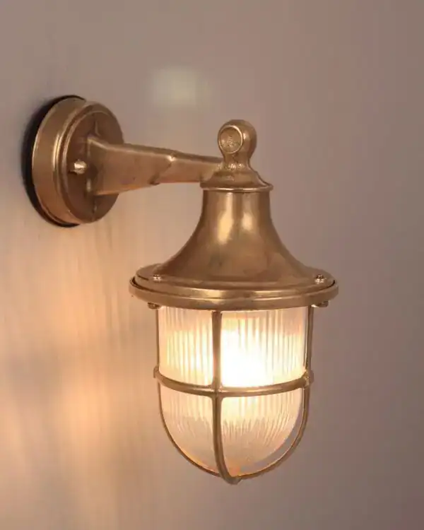 Vintage brass outdoor wall lantern with glass enclosure, illuminated.