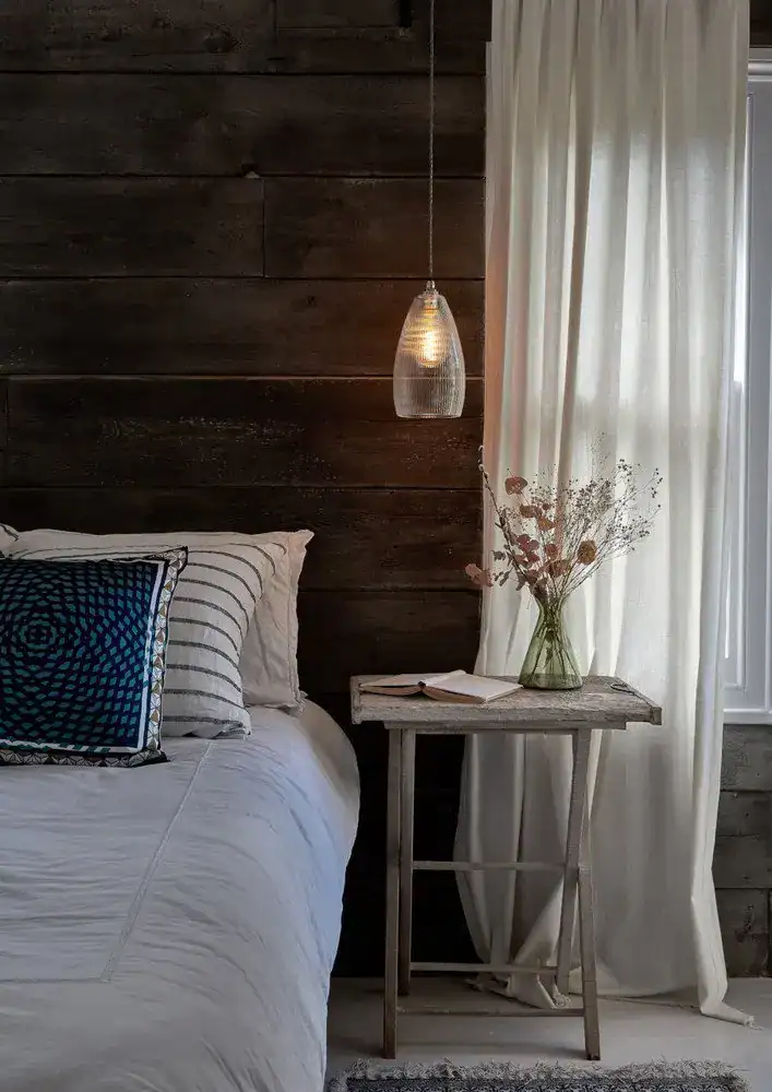 Modern pendant light hanging beside a bed in a cosy bedroom setting.