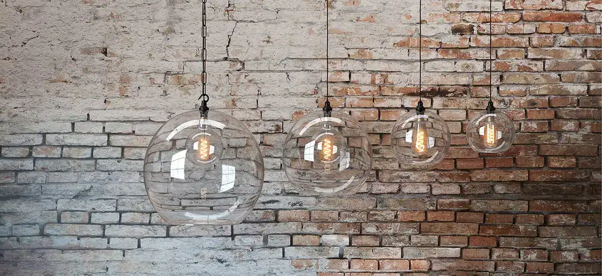 Contemporary glass pendant lights hanging against an exposed brick wall in a stylish interior settin.
