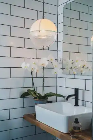 A modern pendant light fixture hanging above a white sink with orchids in a contemporary bathroom.