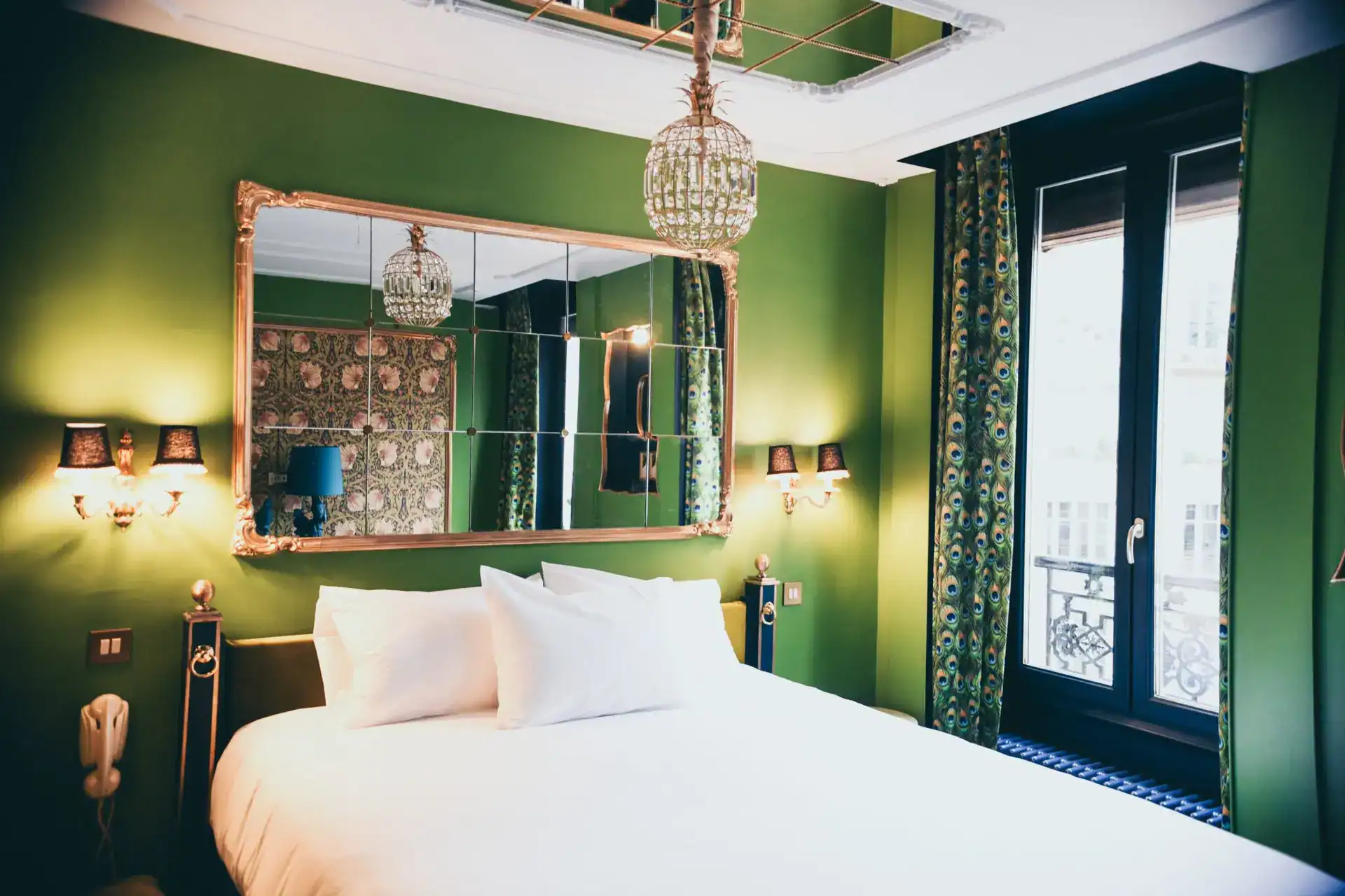 Elegant bedroom with green walls, ornate mirror, chandelier, and modern lighting fixtures.