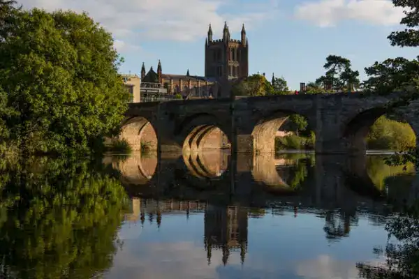 Historic stone bridge over a calm river with a cathedral in the background, in daytime.