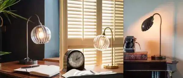 Vintage-style desk lamp illuminating a workspace with books, clock, and camera.