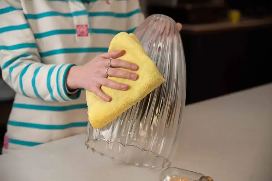Person cleaning glass light fixture with yellow sponge.