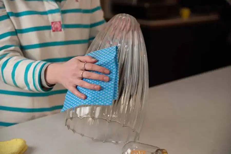 Person cleaning a glass light fixture with a blue cloth in a workshop setting.