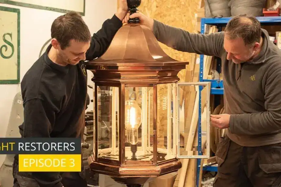 Two craftsmen restoring a vintage lantern-style light fixture in a workshop.