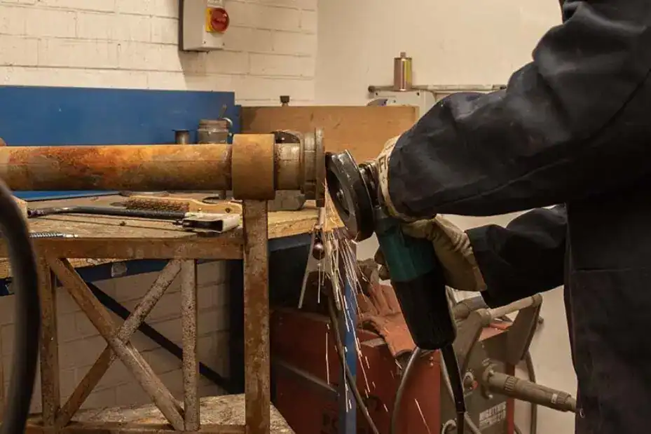 Worker welding metal pipe in workshop.