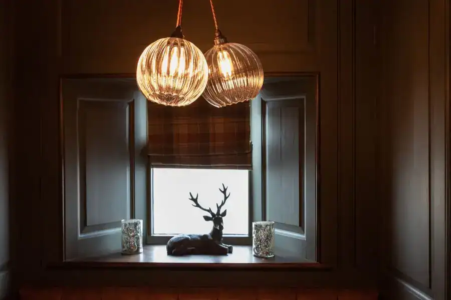 Elegant glass pendant lights hanging above a window with a decorative reindeer silhouette and candle.