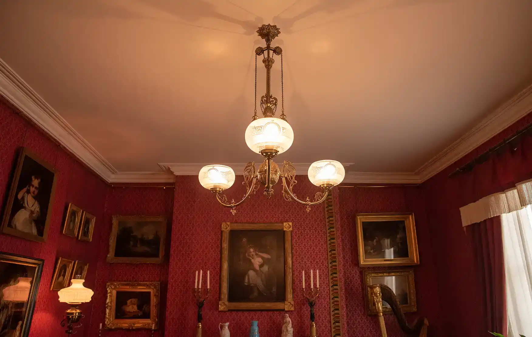 Victorian chandelier with ornate brass details and frosted glass shades hanging in a richly decorate.