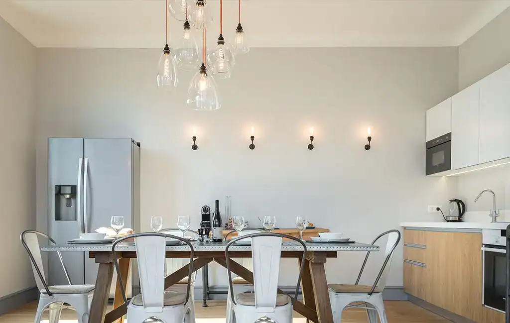 Pendant and wall lights illuminate a contemporary kitchen with a dining area.