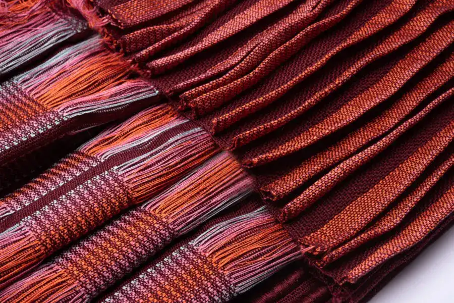 Red and multicolour woven fabric with textured patterns and fringed edges.
