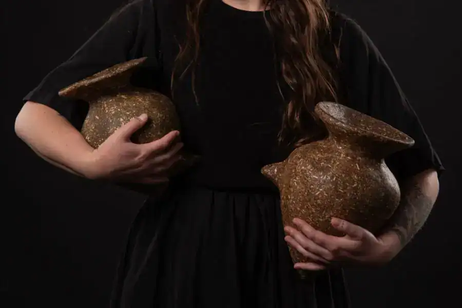 Elegant woman holding two textured ceramic vases against a dark background.