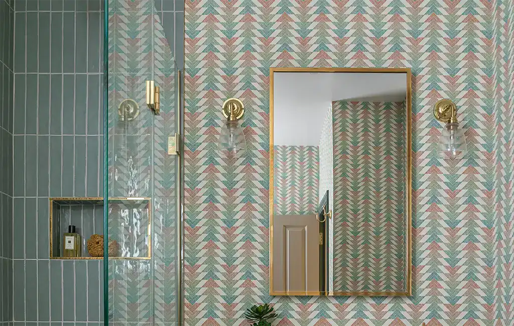 Stylish bathroom wall with colourful geometric wallpaper, gold sconces, and a large mirror.
