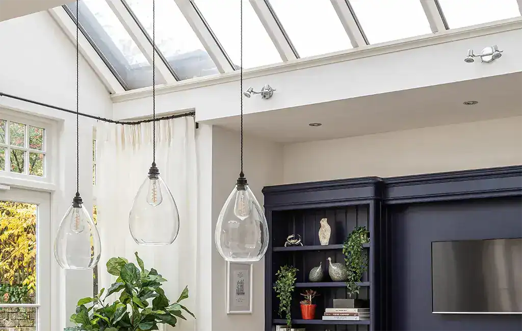 Modern glass pendant lights hanging in a bright, airy living room with large windows and a skylight.