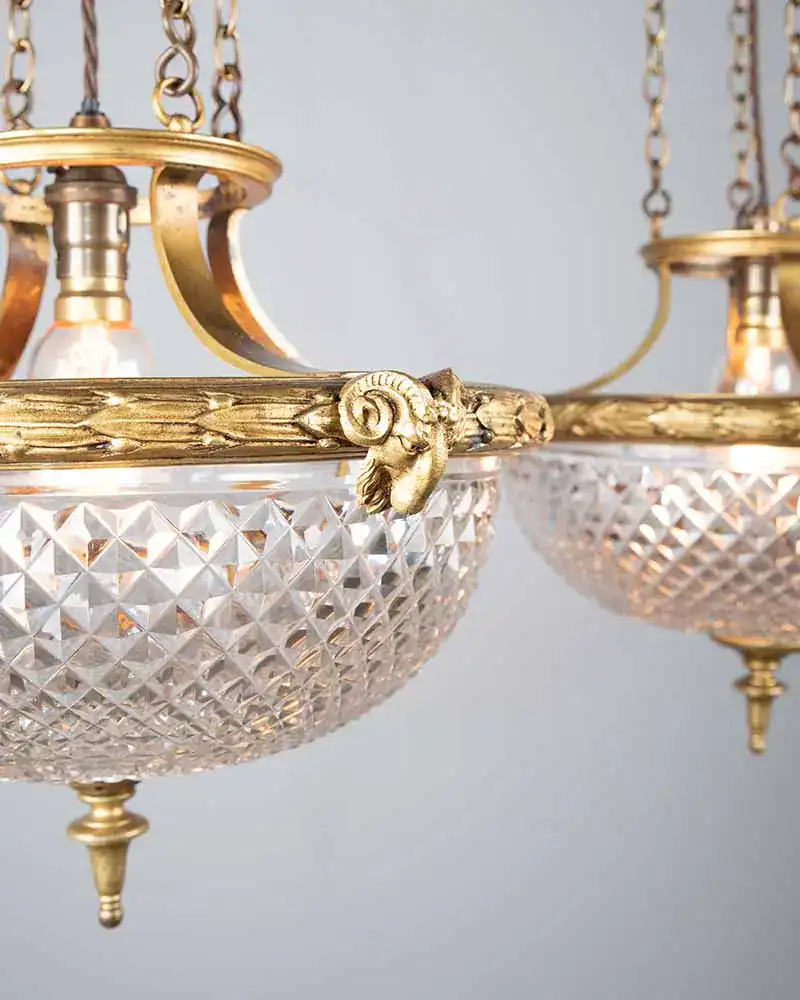 Close-up of a pair of antique cut glass Osler pendants with ornate gilt frames and rams head detailing.