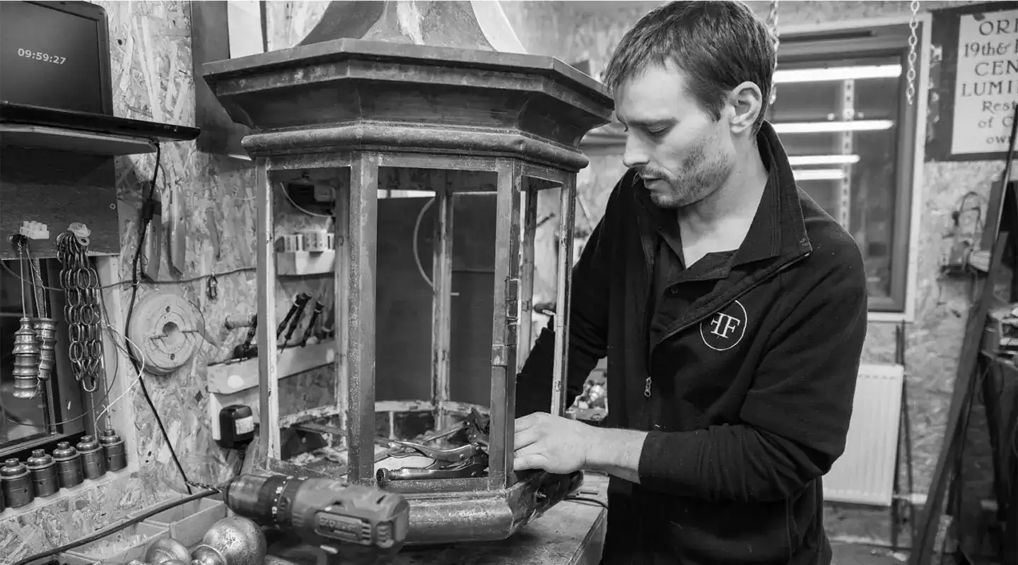 Vintage lantern being repaired by a craftsman in a workshop setting.