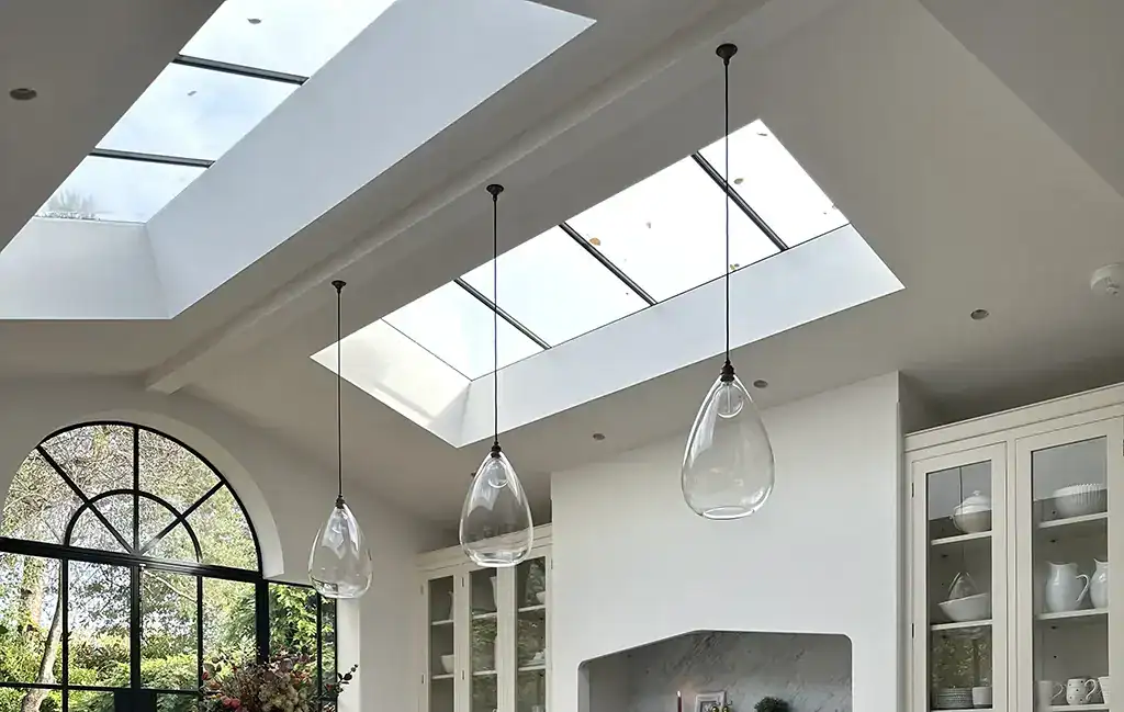 Pendant lights hanging from the ceiling in a bright, modern kitchen with large skylights.