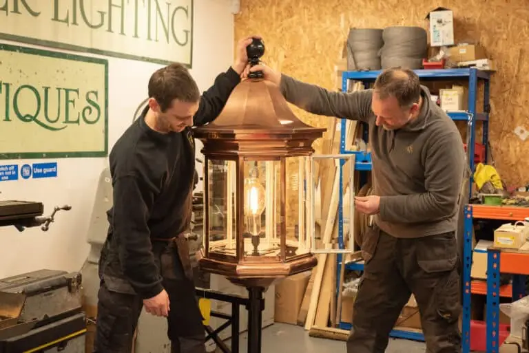 Two men installing a vintage-style outdoor lantern in workshop.